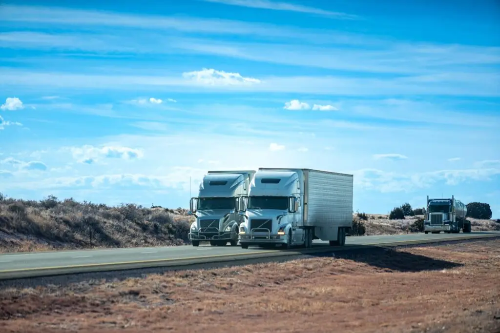 Volvo semi-trucks with enclosed trailers parked on desert highway in New Mexico. Commercial freight transportation fleet at rest stop in arid landscape.
