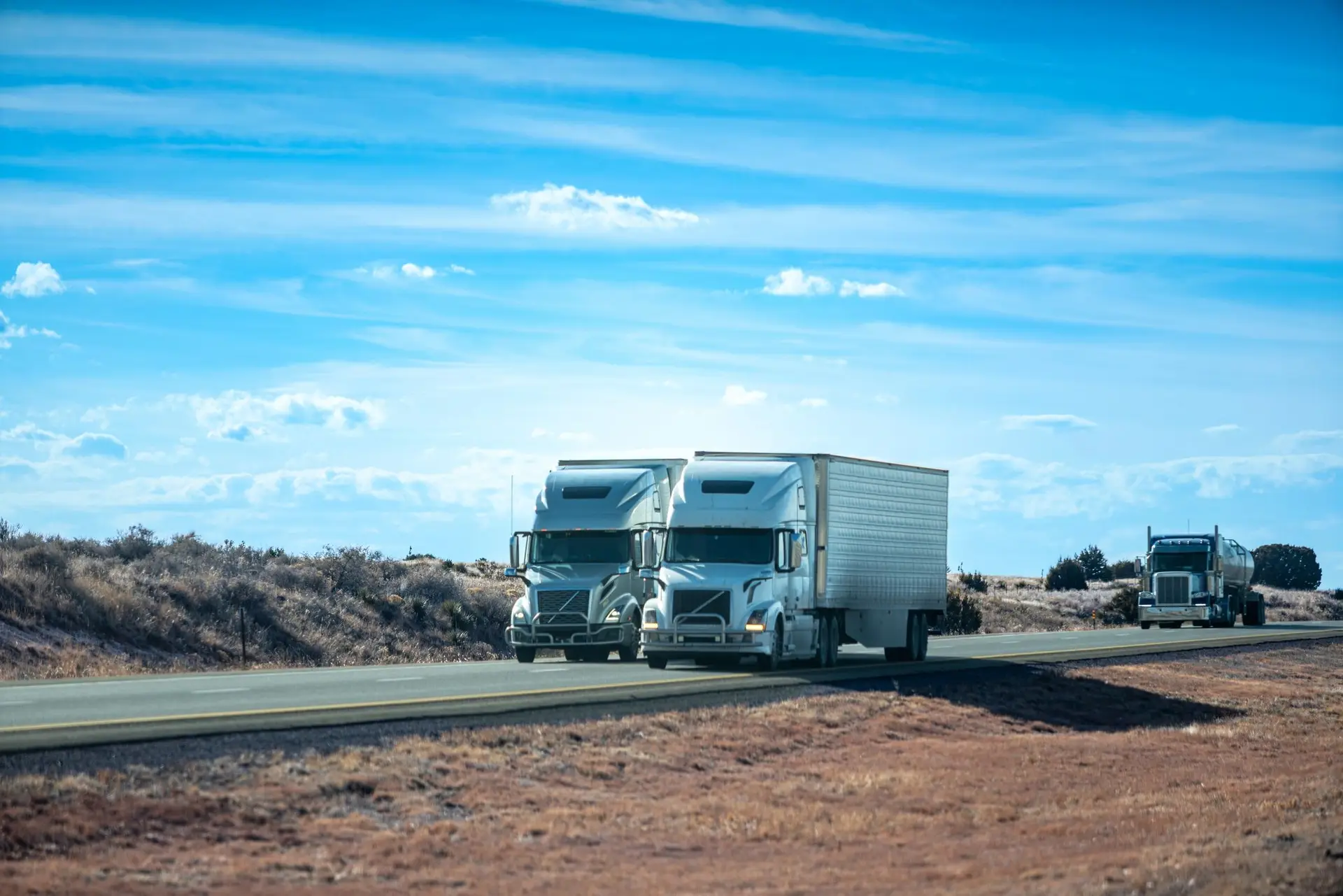 Volvo semi-trucks with enclosed trailers parked on desert highway in New Mexico. Commercial freight transportation fleet at rest stop in arid landscape.